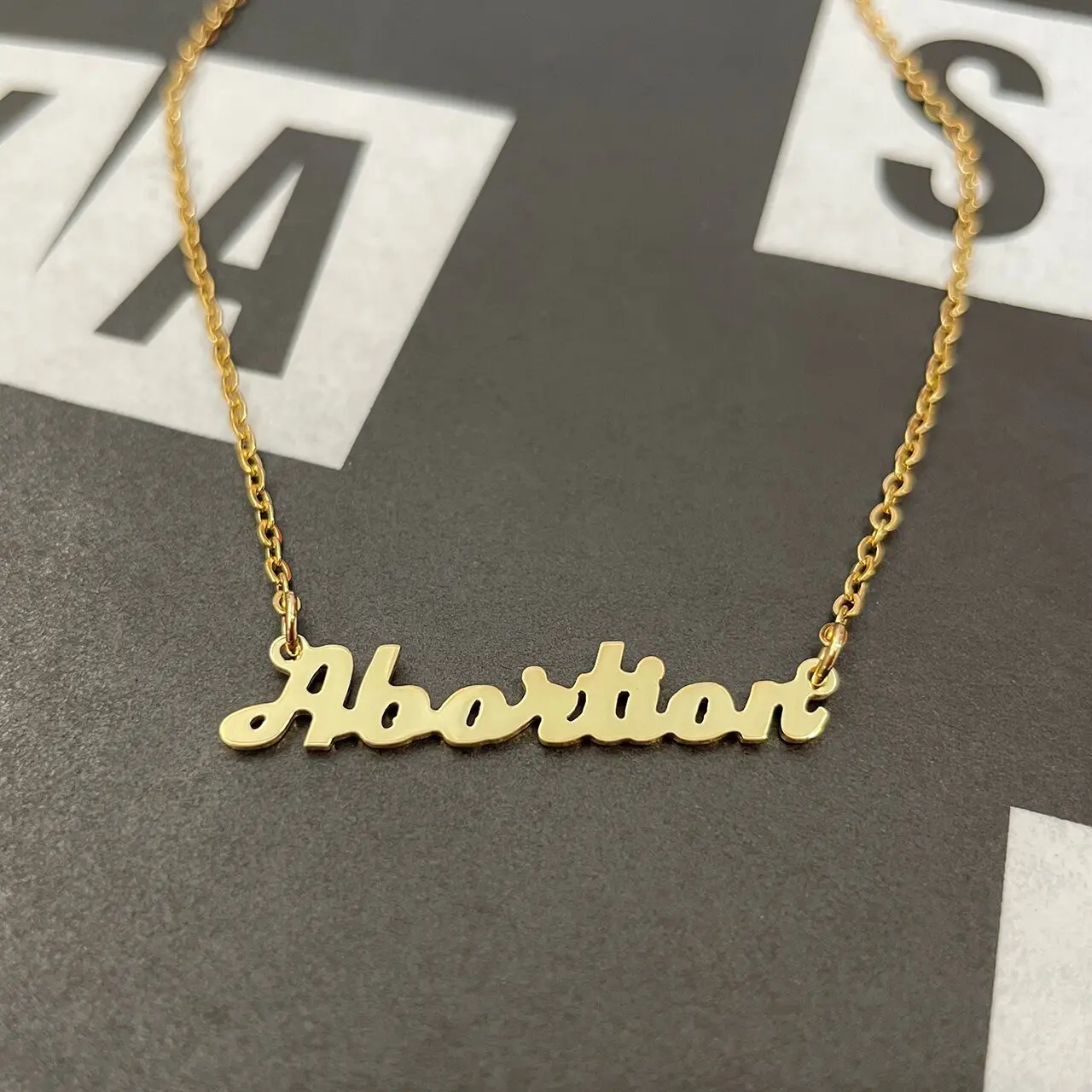 Gold nameplate Abortion necklace on black background