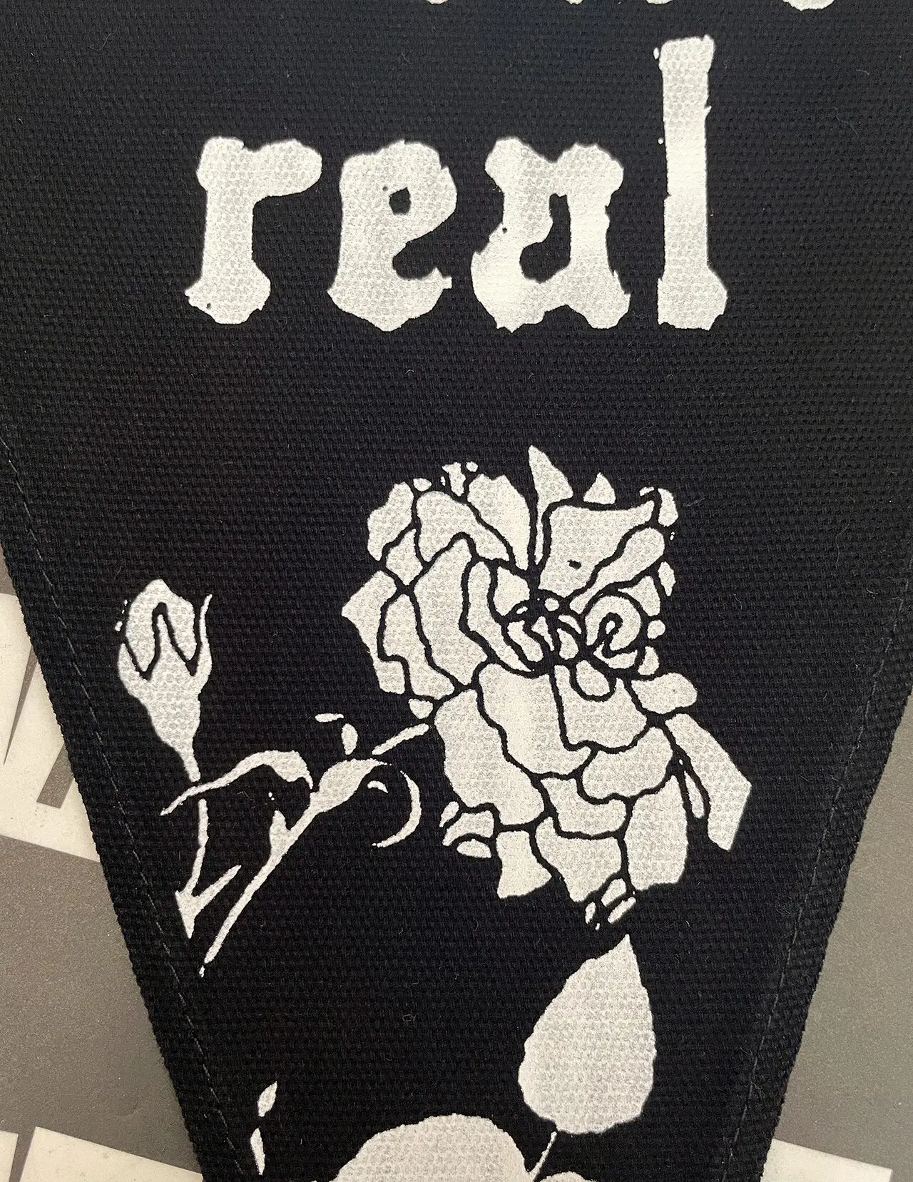 Detail of the Laws Aren't Real pennant flag, focused on the word real and a rose in white ink on the black canvas