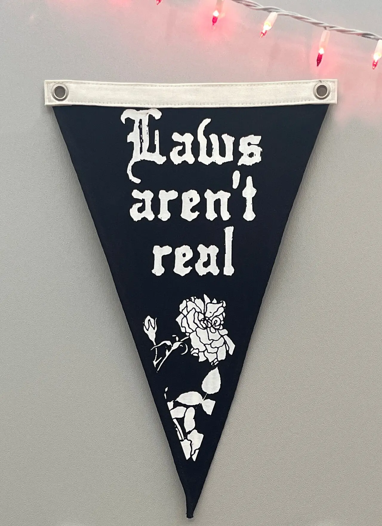 Black canvas triangle pennant with the words Laws Aren't Real and a rose silkscreened on