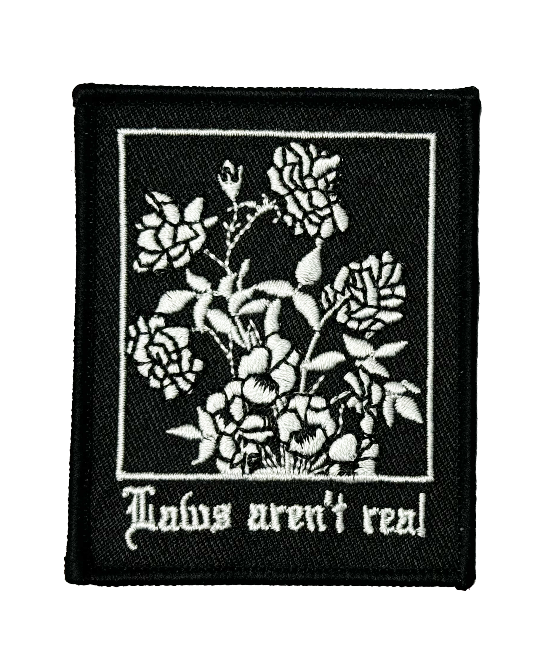 White embroidery on a black patch with flowers and Gothic text "Laws aren't real"