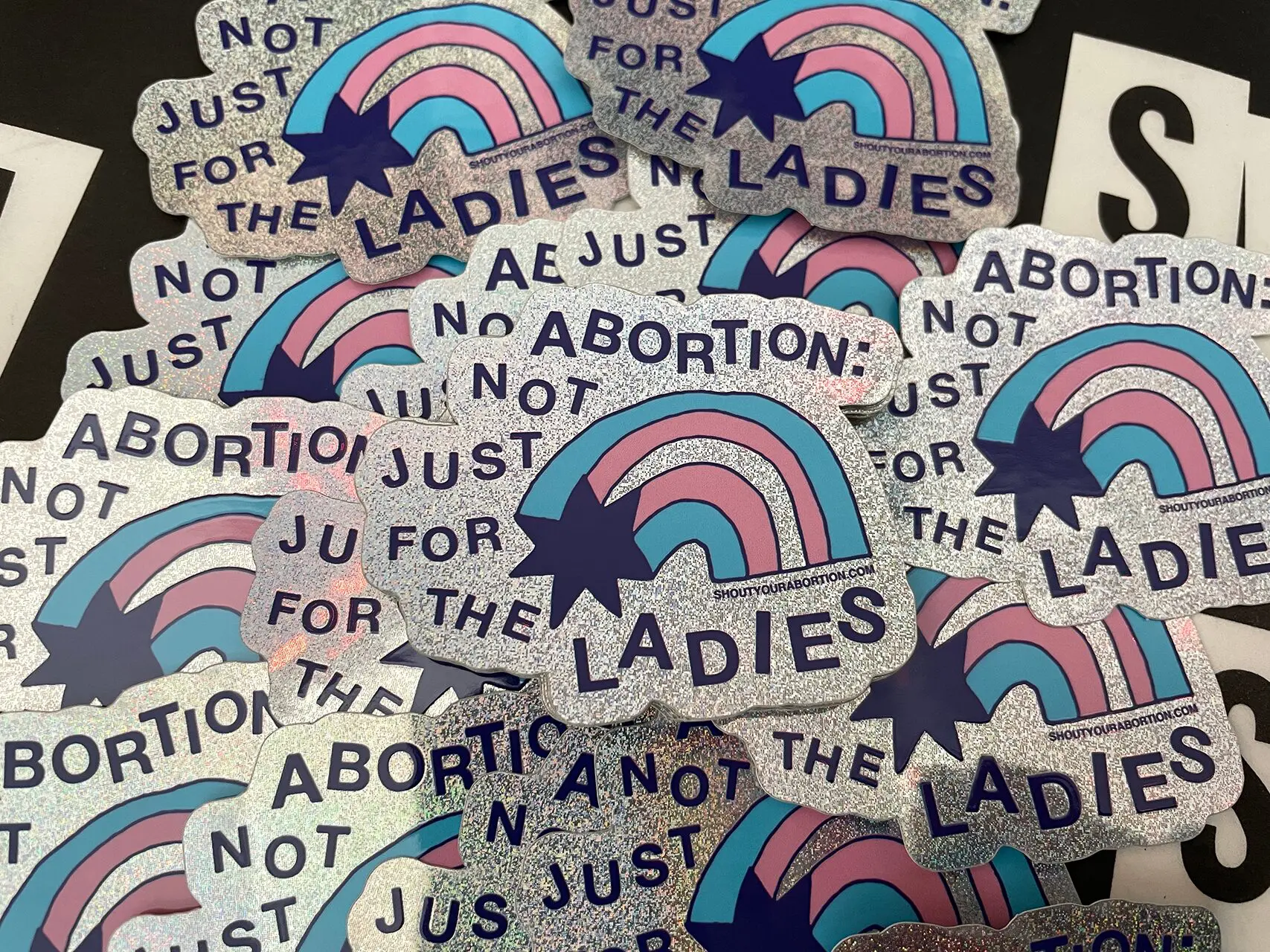 Holographic glitter sticker with a blue, pink and dark blue rainbow and the words ABORTION: NOT JUST FOR THE LADIES