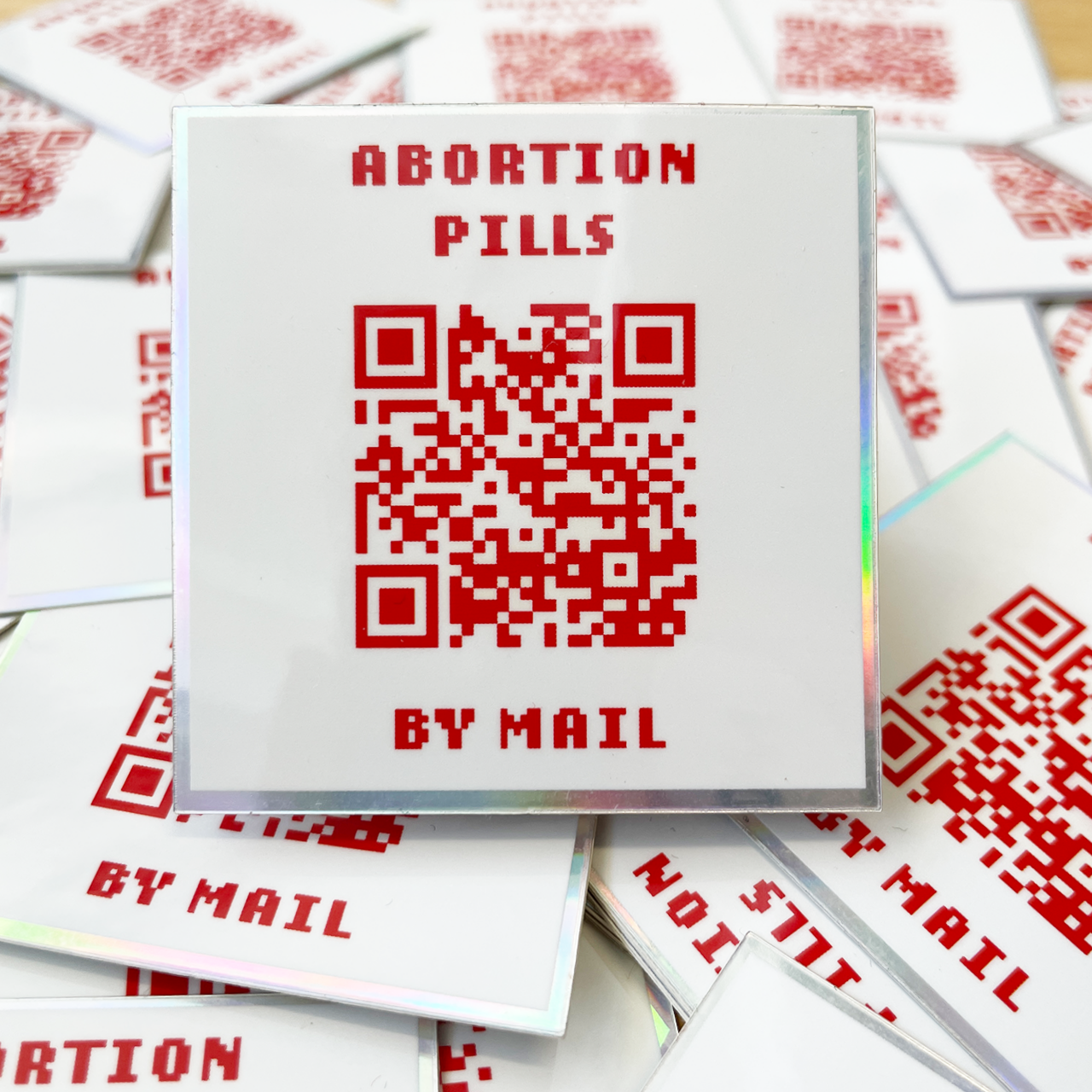 white holographic sticker that says abortion pills by mail with a QR code