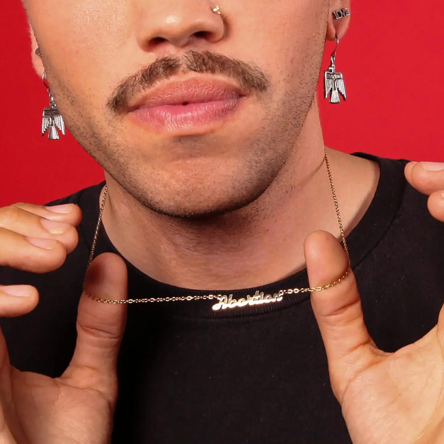 Model with silver earrings, moustache and black tee shirt wearing gold nameplate Abortion necklace