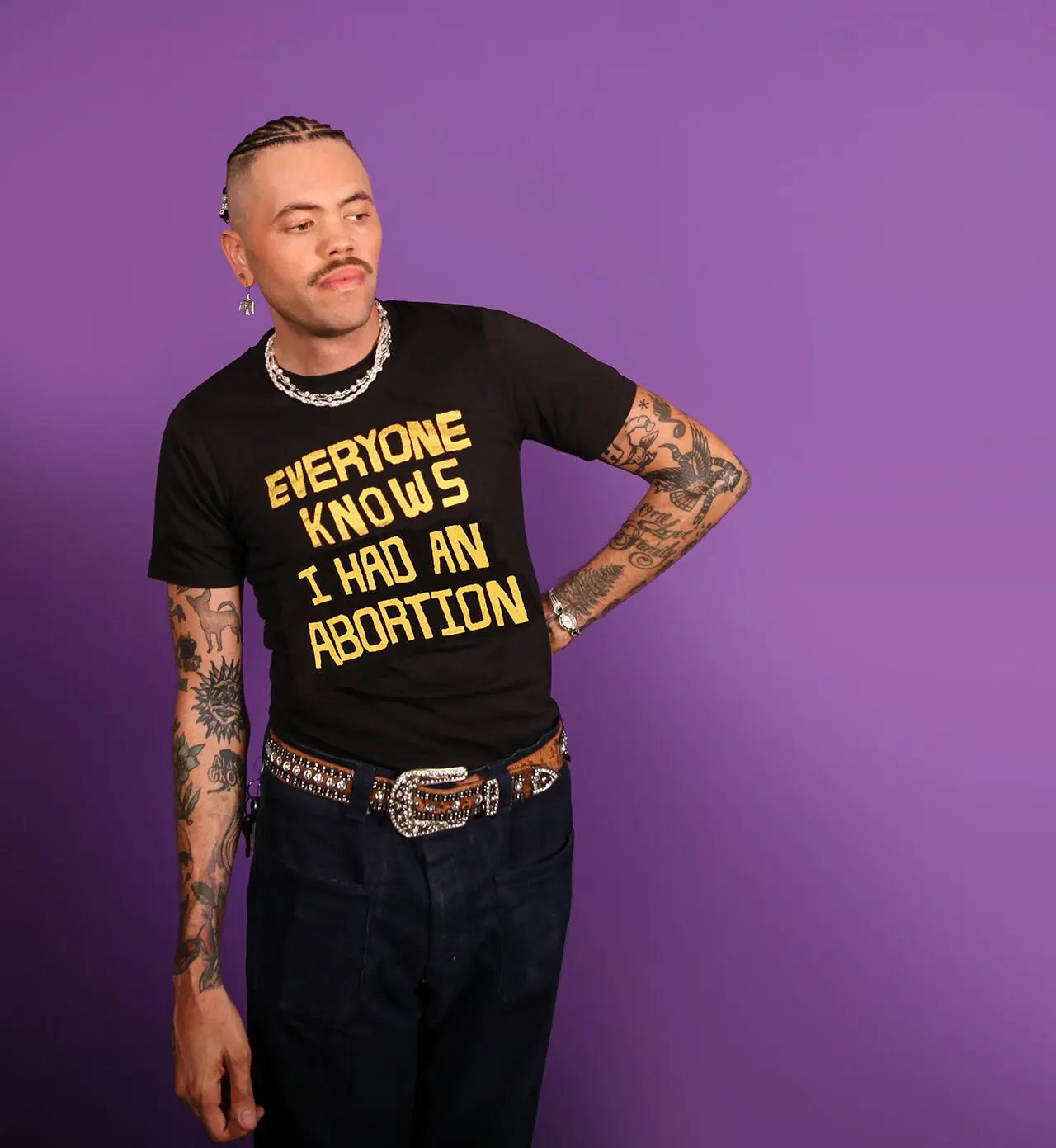 Model wearing a black tee that says EVERYONE KNOWS I HAD AN ABORTION in gold