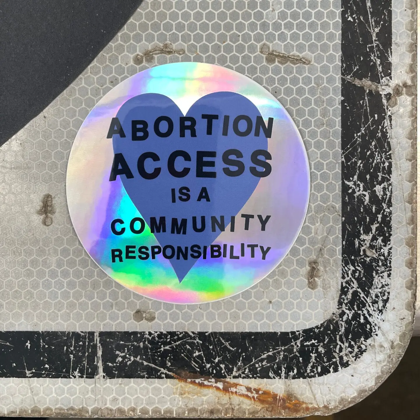 Abortion Access is a Community Responsibility heart holographic sticker on a sign