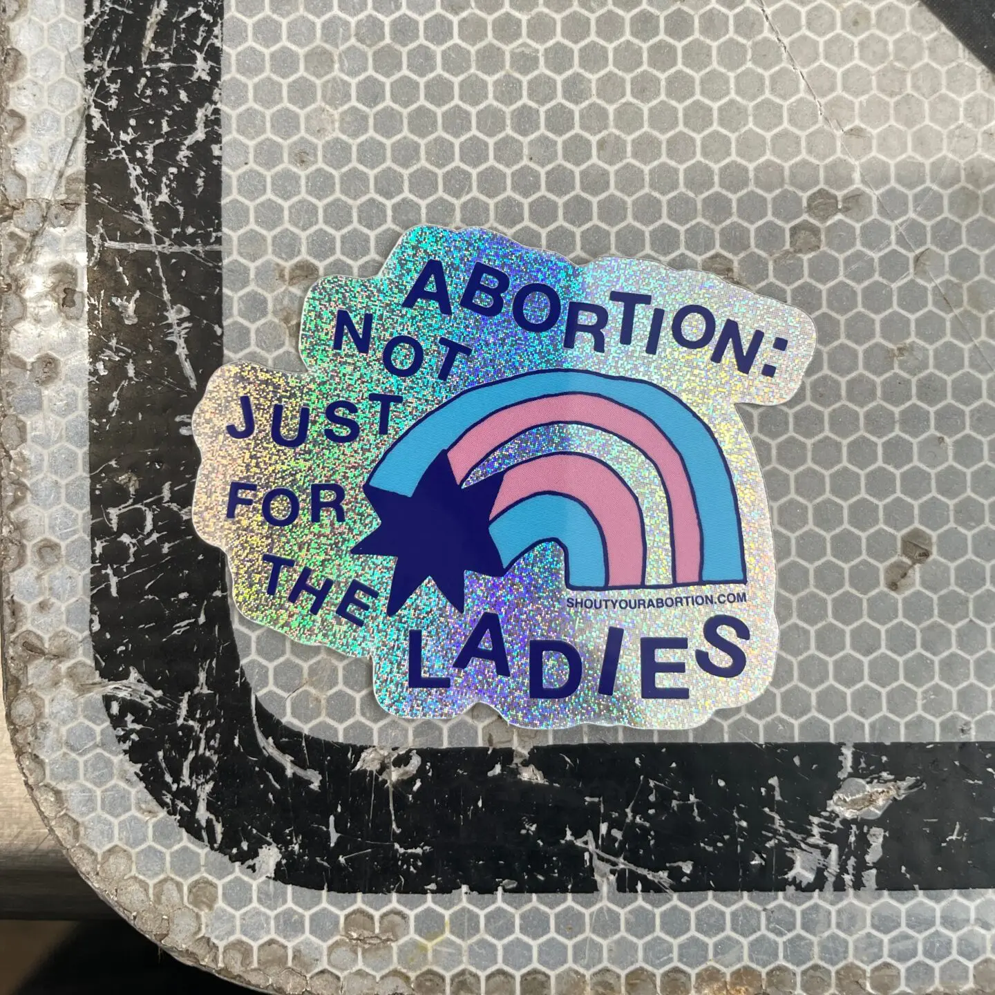 Abortion: Not Just for the Ladies trans rainbow holographic sticker on a sign