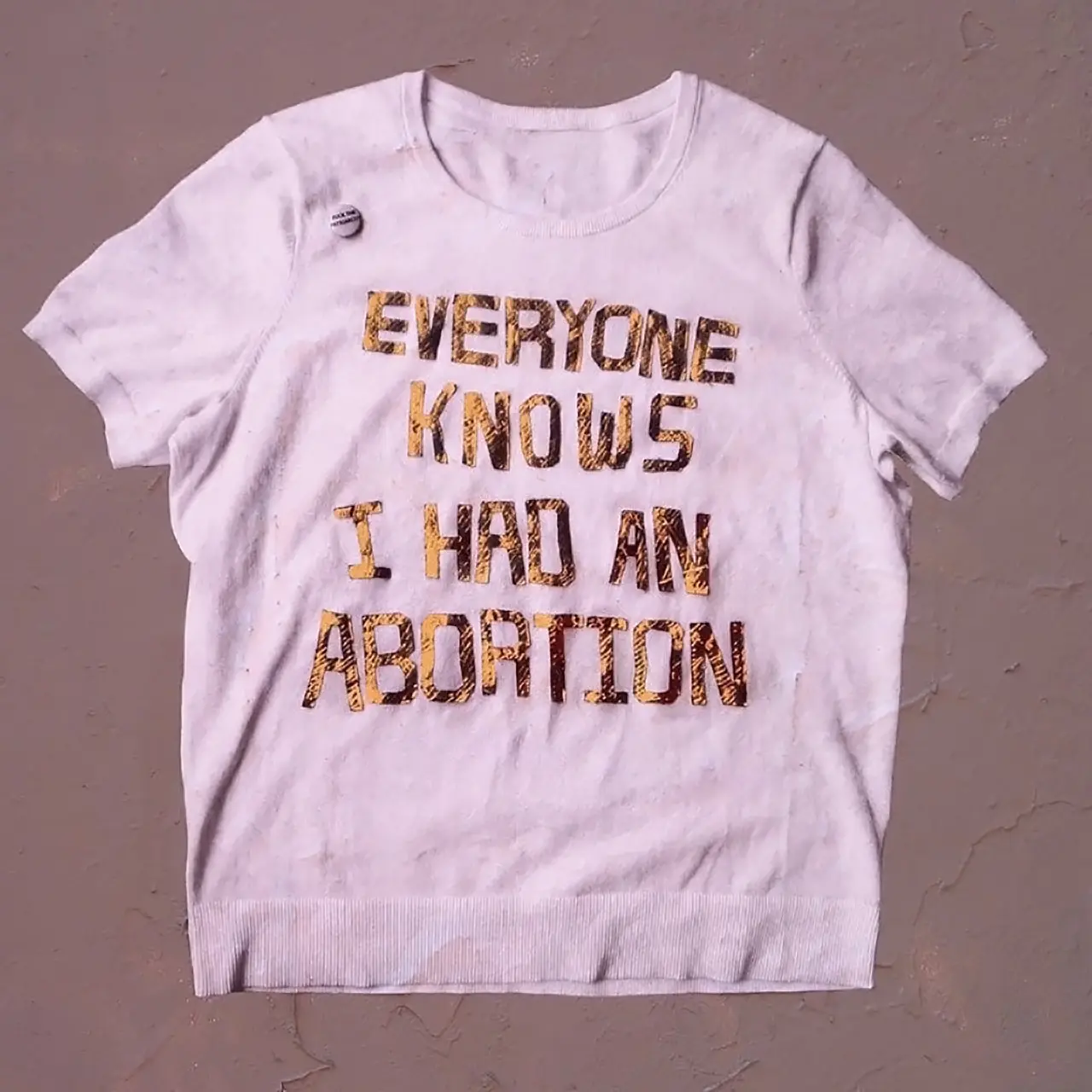 White flat-lay sweater with the words Everyone Knows I had an Abortion in gold on the front