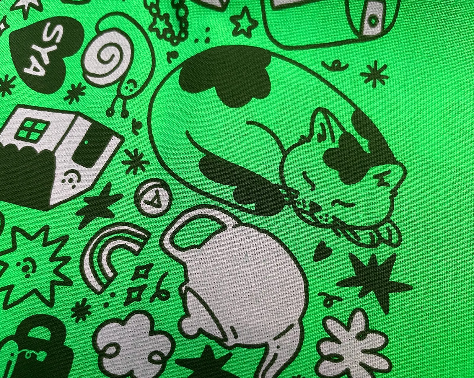 Close up of green bandana with black and light purple screenprinting, focused on a sleeping kitty