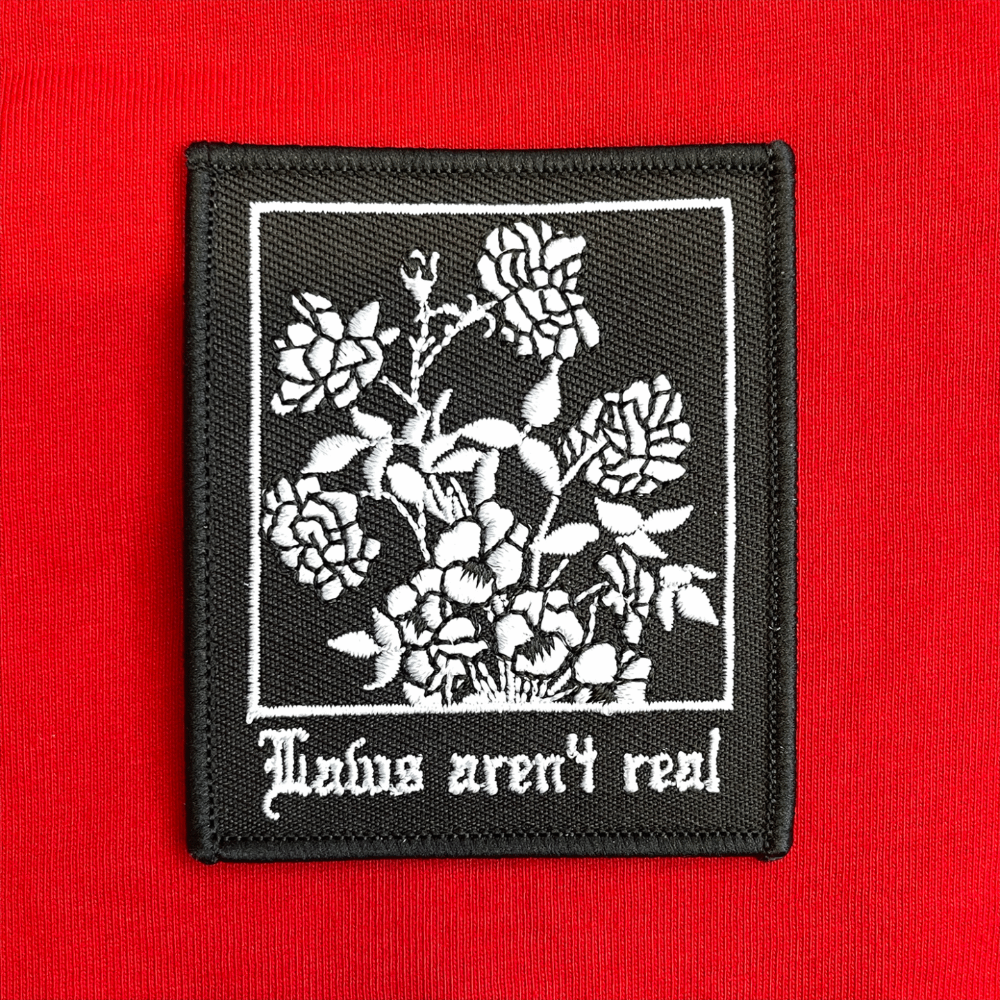White embroidery on a black background reading Laws aren't real with a graphic of roses