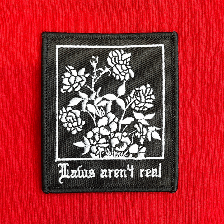 White embroidery on a black background reading Laws aren't real with a graphic of roses